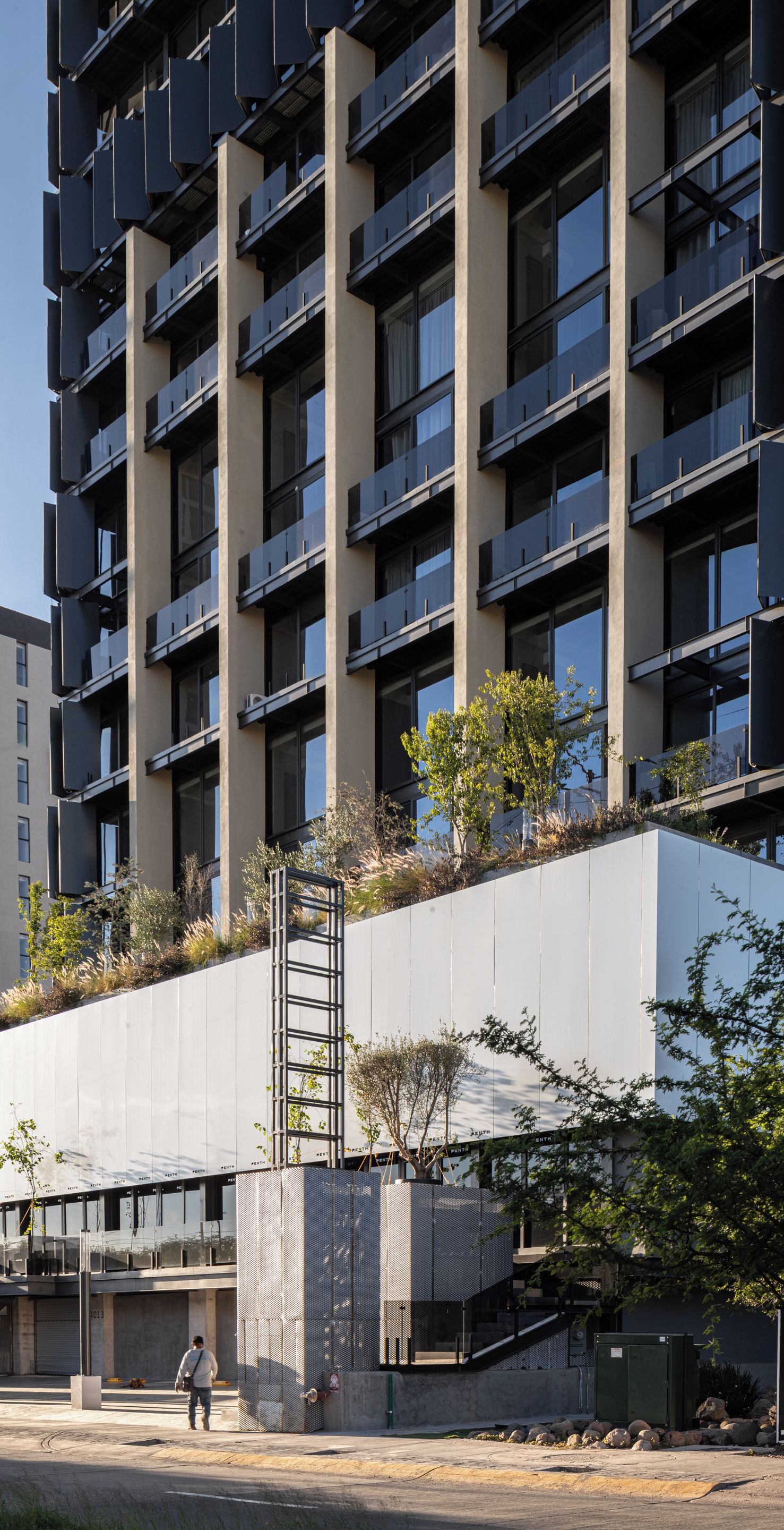Un edificio de varios pisos con balcones, un paseo cubierto y una zona ajardinada con árboles.