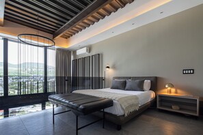 Un dormitorio moderno con una cama grande, un banco, una mesita de noche y vistas a la ciudad.