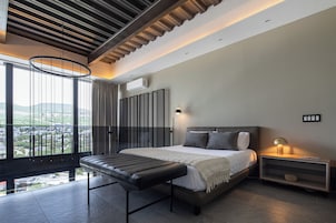 Un dormitorio moderno con una cama grande, un banco, una mesita de noche y vistas a la ciudad.