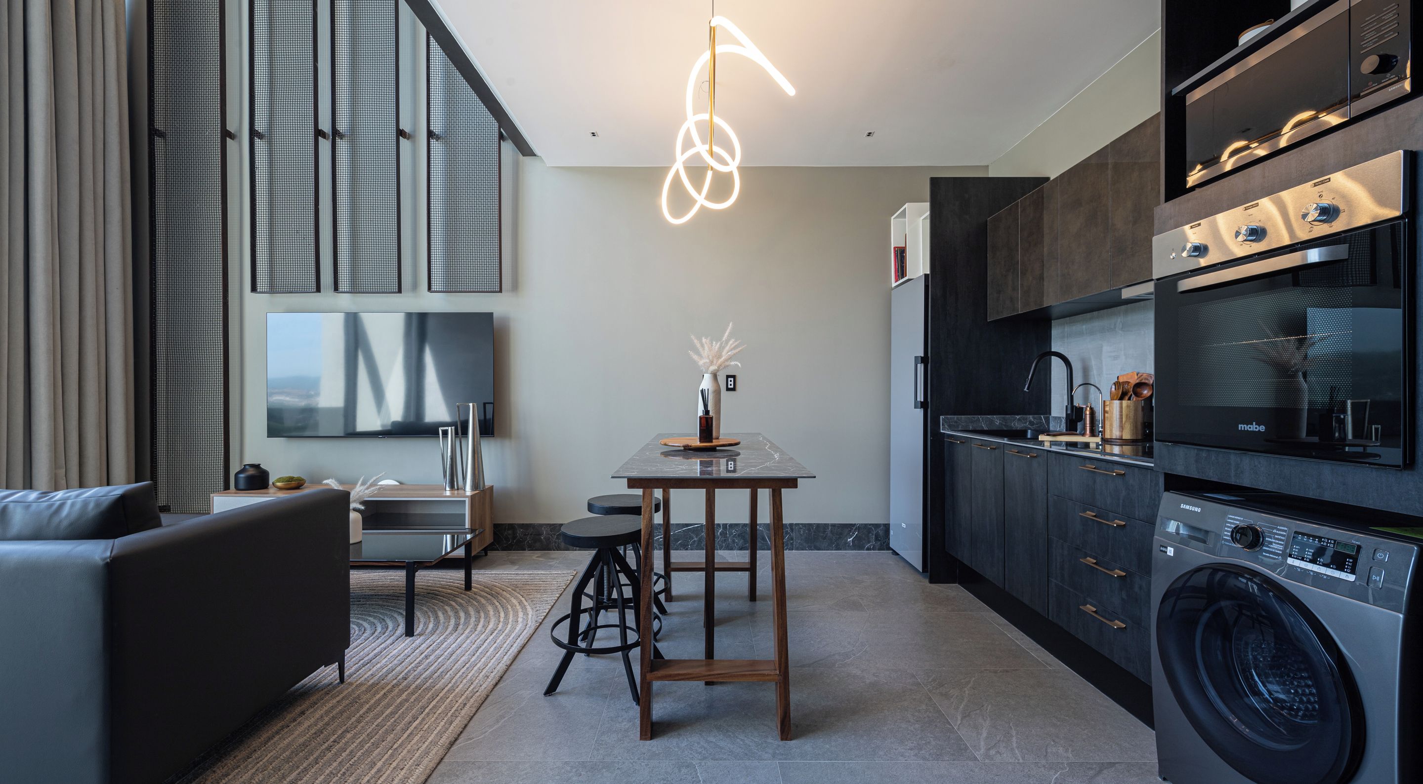A modern kitchen with a built-in washer and dryer, a dining area with a table and chairs, and a living room with a sofa and a TV.