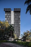 Un edificio moderno con fachada enrejada, rodeado de follaje y árboles.
