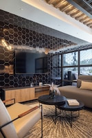 A modern living room with a large flat-screen TV, a sofa, a coffee table, and a patterned rug.