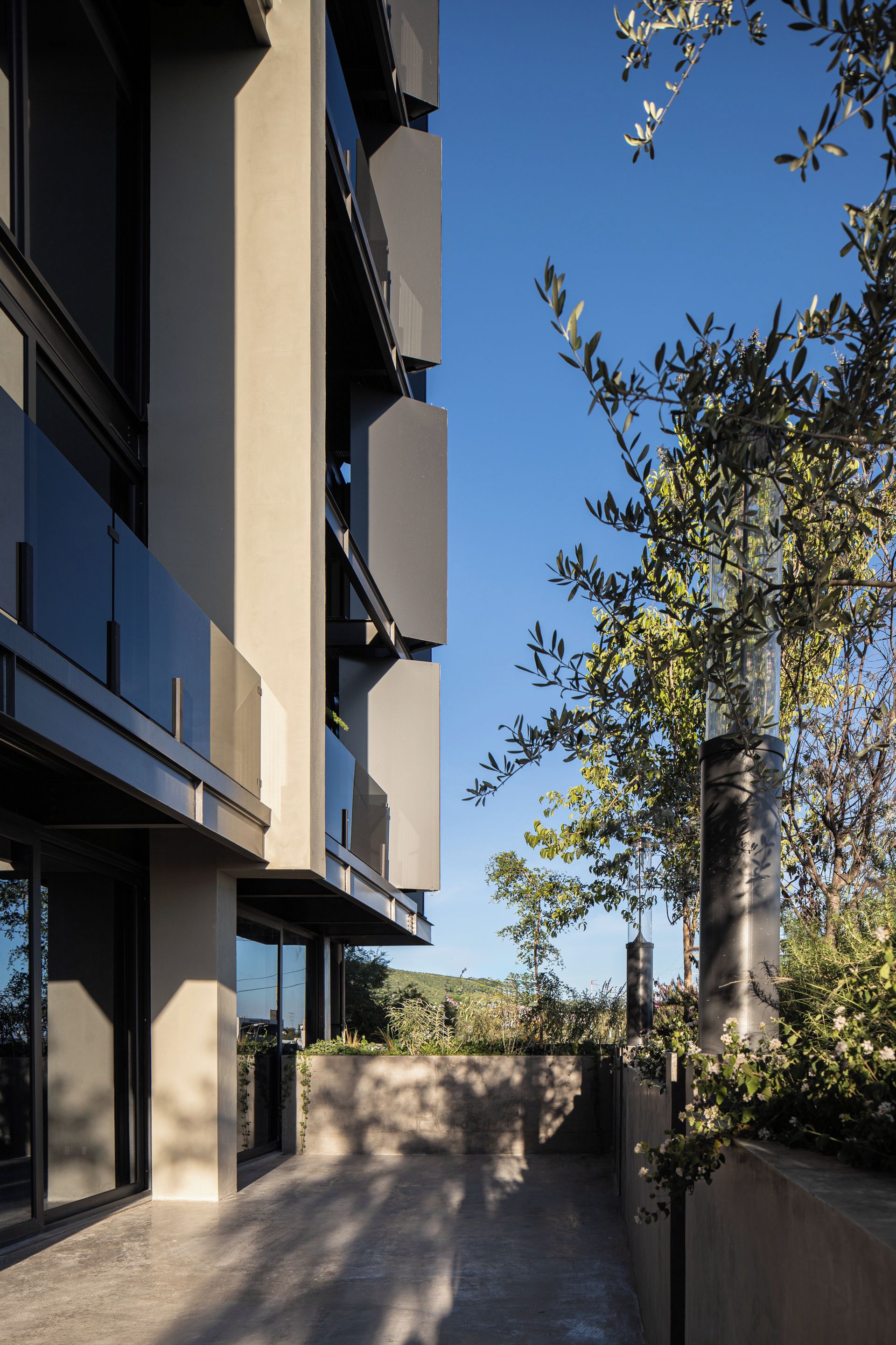 A modern building with a concrete facade, large windows, and a balcony overlooking a garden.