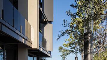 A modern building with a concrete facade, large windows, and a balcony overlooking a garden.