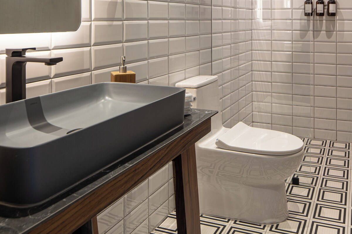 A modern bathroom with a large mirror, a vessel sink, a toilet, and a shower area.