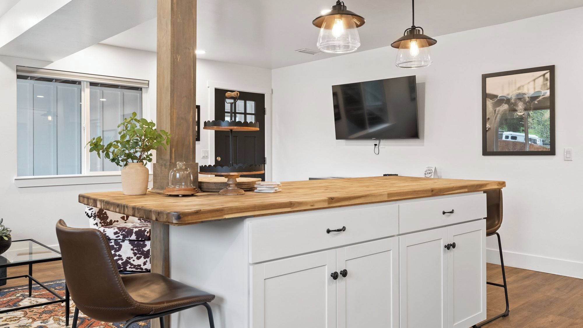 Una cocina moderna con una isla de madera, armarios blancos y un televisor de pantalla plana montado encima.