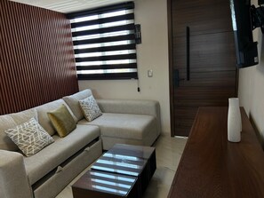 A modern living room with a sectional sofa, a coffee table, and a wooden dining table. - LESLIEES HOUSE (Zapopan)