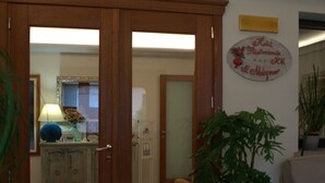 A hotel room with a wooden door, a potted plant, a sofa, and a wall sign. - Hotel Ristorante Il Melograno (Nuchis)