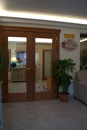 A hotel room with a wooden door, a potted plant, a sofa, and a wall sign. - Hotel Ristorante Il Melograno (Nuchis)