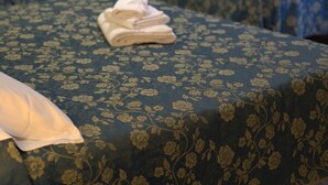 A hotel room with two beds, each with a floral-patterned bedspread, a folded towel on the first bed, and a framed picture on the wall. - Hotel Ristorante Il Melograno (Nuchis)