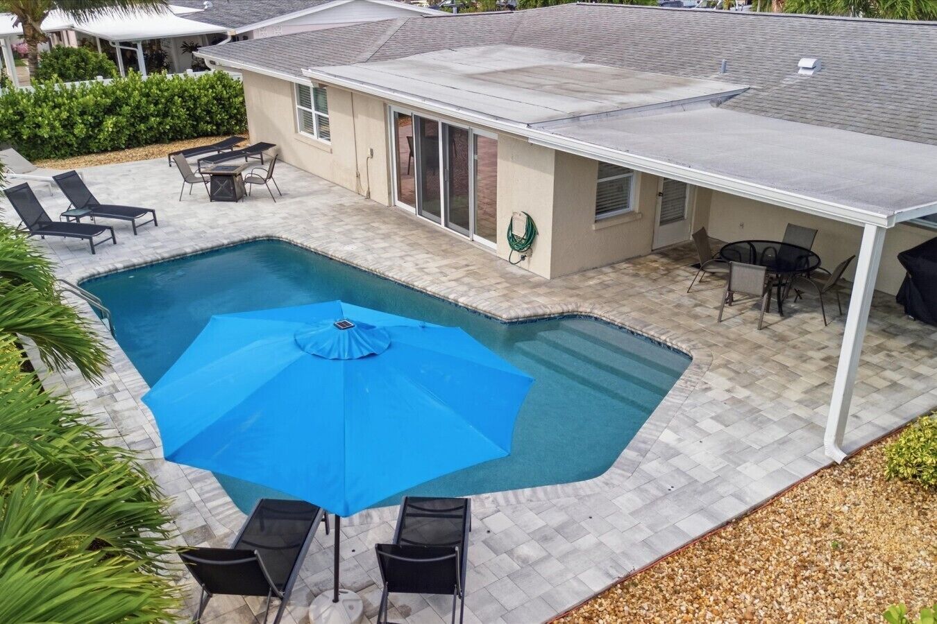 Ein Swimmingpool mit blauem Sonnenschirm, umgeben von Liegestühlen und einem Patio-Tisch.