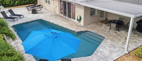 Ein Swimmingpool mit blauem Sonnenschirm, umgeben von Liegestühlen und einem Patio-Tisch.