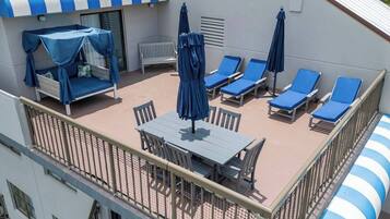 Une terrasse sur le toit avec une table et des chaises, des chaises longues avec des parasols et un espace salon couvert.