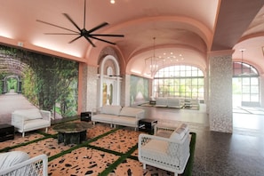 Uma sala de estar espaçosa com um ventilador de teto moderno, um mural grande e um conjunto de assentos incluindo um sofá e duas poltronas.