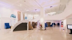 En rummelig lobby med en central trappe, siddepladser og en lysekrone.
