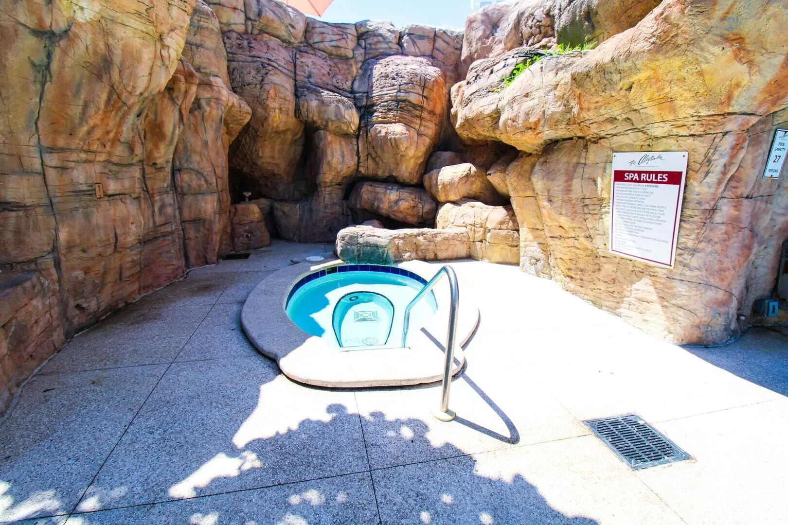 Uma pequena piscina interior com escada de metal, rodeada por paredes rochosas, e um aviso com as regras do spa.