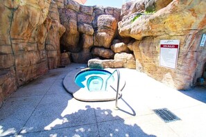 Uma pequena piscina interior com escada de metal, rodeada por paredes rochosas, e um aviso com as regras do spa.