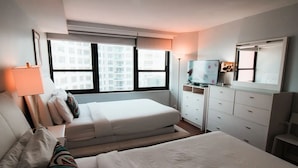 Et hotelværelse med seng, natbord, lampe, kommode og fjernsyn.