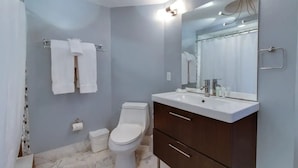 Et badeværelse med toilet, håndvask, spejl og håndklædestang.