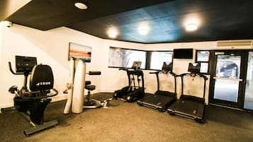 Uma academia com equipamentos de exercícios, incluindo esteira, elíptico e máquina de pesos.