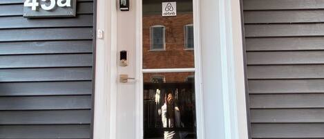 A front door with a number plate, a glass door, and a brick wall behind it.