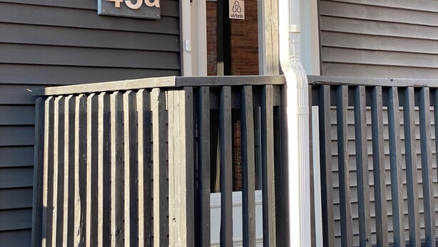 A house with a porch, a door with a sign, and a number sign indicating the address.