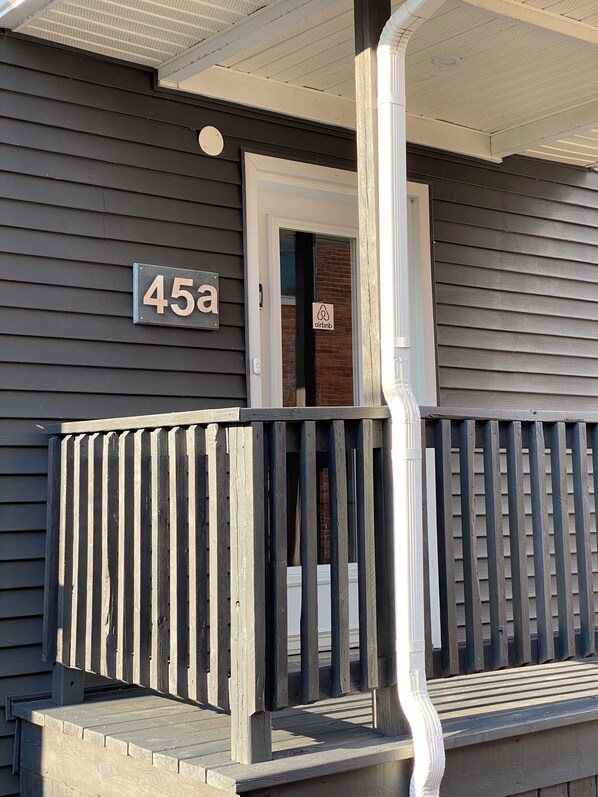 A house with a porch, a door with a sign, and a number sign indicating the address.
