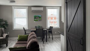 A modern living room with a sofa, chairs, a dining table, and a large window.