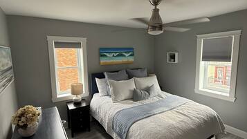 Une chambre à coucher avec un lit, des tables de chevet, un ventilateur de plafond et une fenêtre donnant sur un beau paysage.