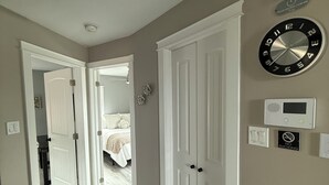 A hallway with a white door, a clock, a smoke detector, and a thermostat. - Executive Guest 45N (North Glengarry)