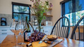 Une table en bois, une bouteille de vin, deux verres, un bol de raisins, un couteau à fromage et une planche en bois avec des crackers.