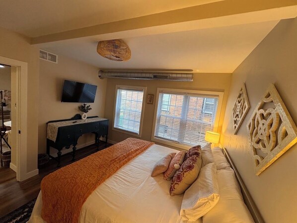 Un dormitorio con cama, escritorio, televisor y ventana con persianas.