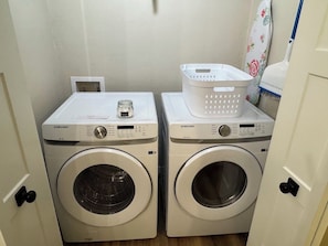 Two Samsung washing machines in a laundry room with a white basket on top of one. - Monroe Lofts Suite 1 Downtown 2BR Apartment (Green Bay)