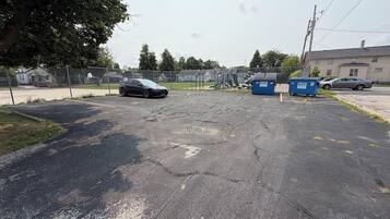 A parking lot with a damaged asphalt surface, a chain-link fence, and dumpsters labeled 'BWS'.