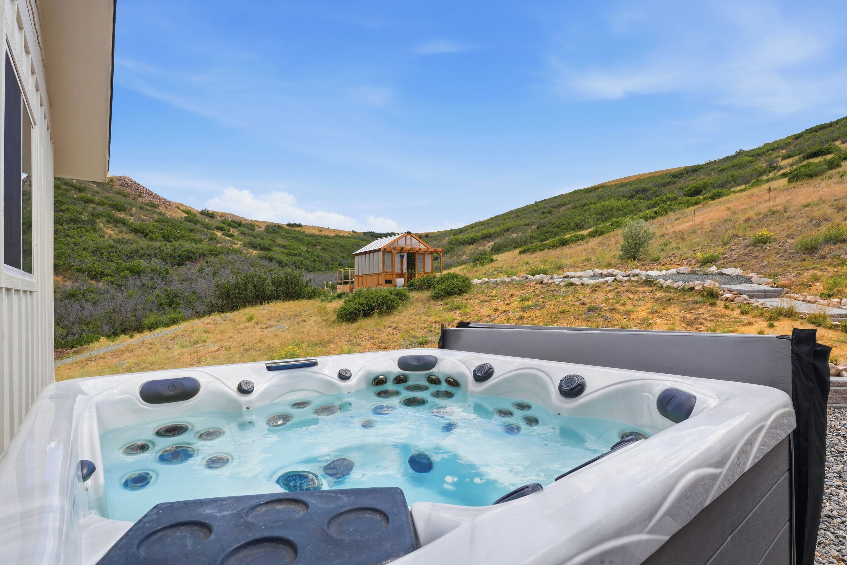 Ein Whirlpool mit Blick auf eine Hügellandschaft und einem Holzgebäude im Hintergrund.