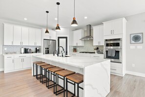 A modern kitchen with white cabinetry, a central island with bar stools, stainless steel appliances, and pendant lighting. - Peaceful|Hot Tub|Sauna|Close to Downtown (Castle Rock)