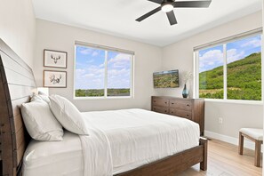 A bedroom with a bed, a dresser, a chair, and two windows with a view of a green landscape. - Peaceful|Hot Tub|Sauna|Close to Downtown (Castle Rock)