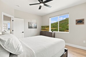 Ein Schlafzimmer mit einem Bett, einem Deckenventilator, einem Fenster mit Blick auf eine Landschaft und Kunstwerken an der Wand.