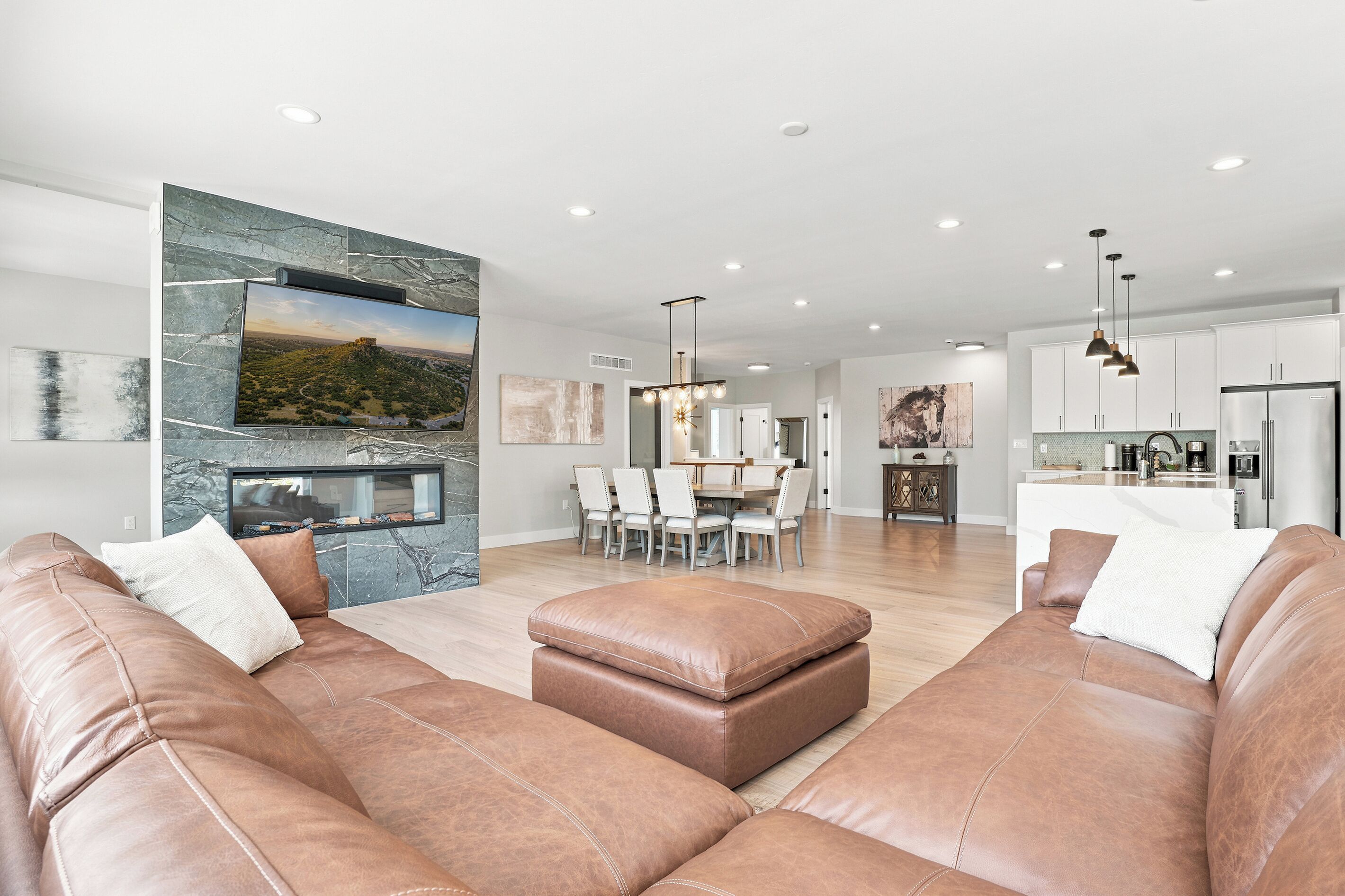 A modern living room with leather sofas, a flat-screen TV, and a dining area with a chandelier.