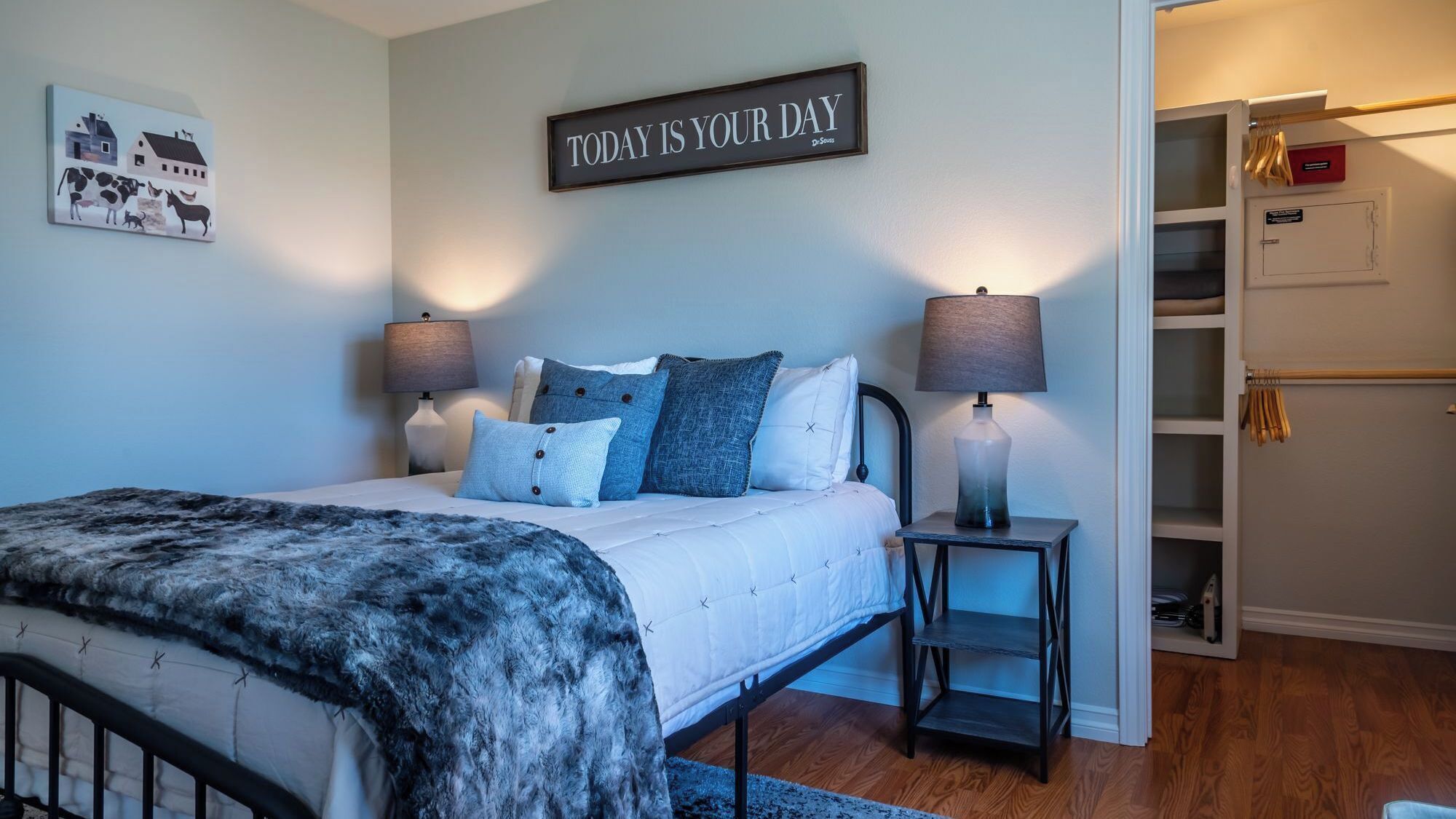 A bedroom with a bed, two bedside lamps, a bedside table, a wall-mounted sign, and a wardrobe.