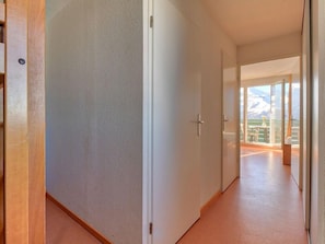 Un pasillo con una puerta de madera a la izquierda, una puerta blanca en el centro y vista a un balcón con una montaña al fondo.