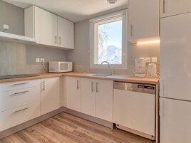 Una cocina moderna con armarios blancos, microondas, lavavajillas y ventana con vistas a montañas.