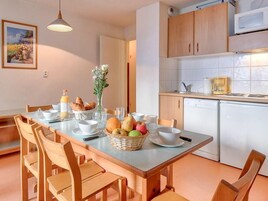 A dining area with a table set for two, a kitchen with white appliances, and wooden cabinets.