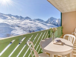 Un balcón con vistas a montañas nevadas, una mesa redonda y dos sillas.