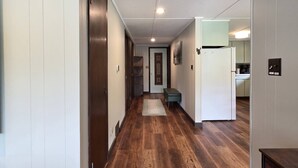 A hallway with wooden flooring, a bench, and a refrigerator in the kitchen area. - Cabin with Private Pond - 61 Acres - Close to Gore (Johnsburg)