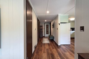 A hallway with wooden flooring, a bench, and a refrigerator in the kitchen area. - Cabin with Private Pond - 61 Acres - Close to Gore (Johnsburg)