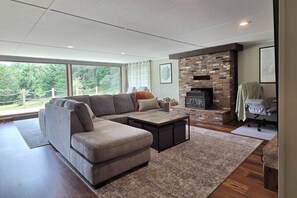 A modern living room with a sectional sofa, a coffee table, and a fireplace. - Cabin with Private Pond - 61 Acres - Close to Gore (Johnsburg)