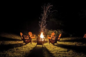 A campfire with two Adirondack chairs facing it, set on a grassy area at night. - Cabin with Private Pond - 61 Acres - Close to Gore (Johnsburg)