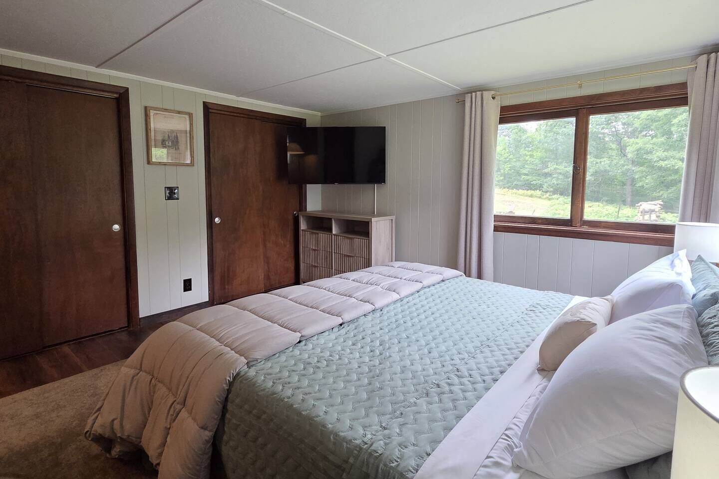 A bedroom with a bed, a television, a window with curtains, and a door.
