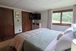 A bedroom with a bed, a television, a window with curtains, and a door. - Cabin with Private Pond - 61 Acres - Close to Gore (Johnsburg)